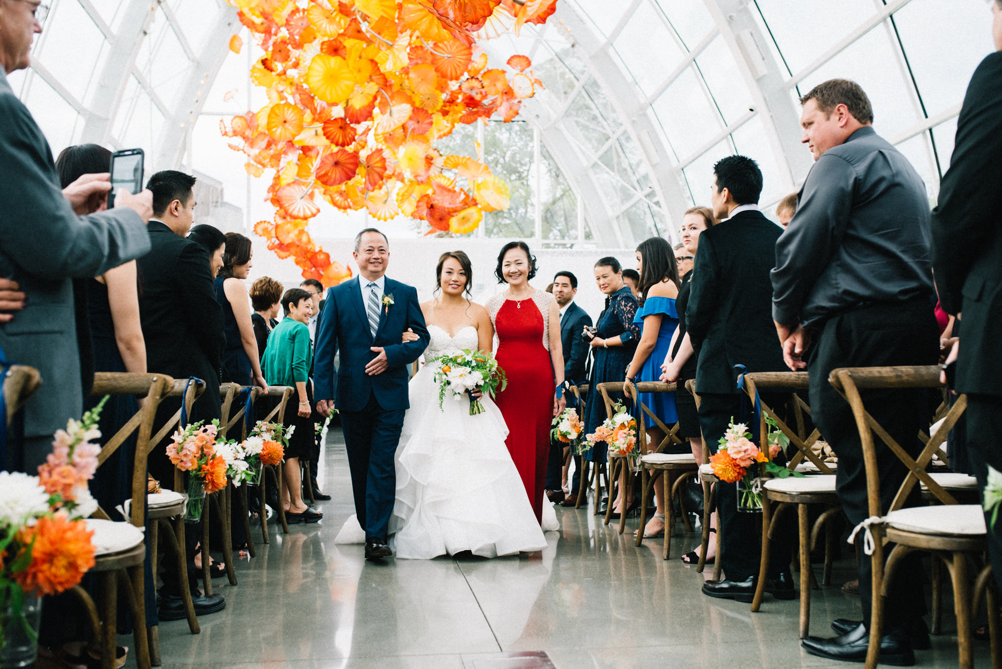 Amy walks down the aisle with her parents at her wedding ceremony at Chihuly Garden and Glass