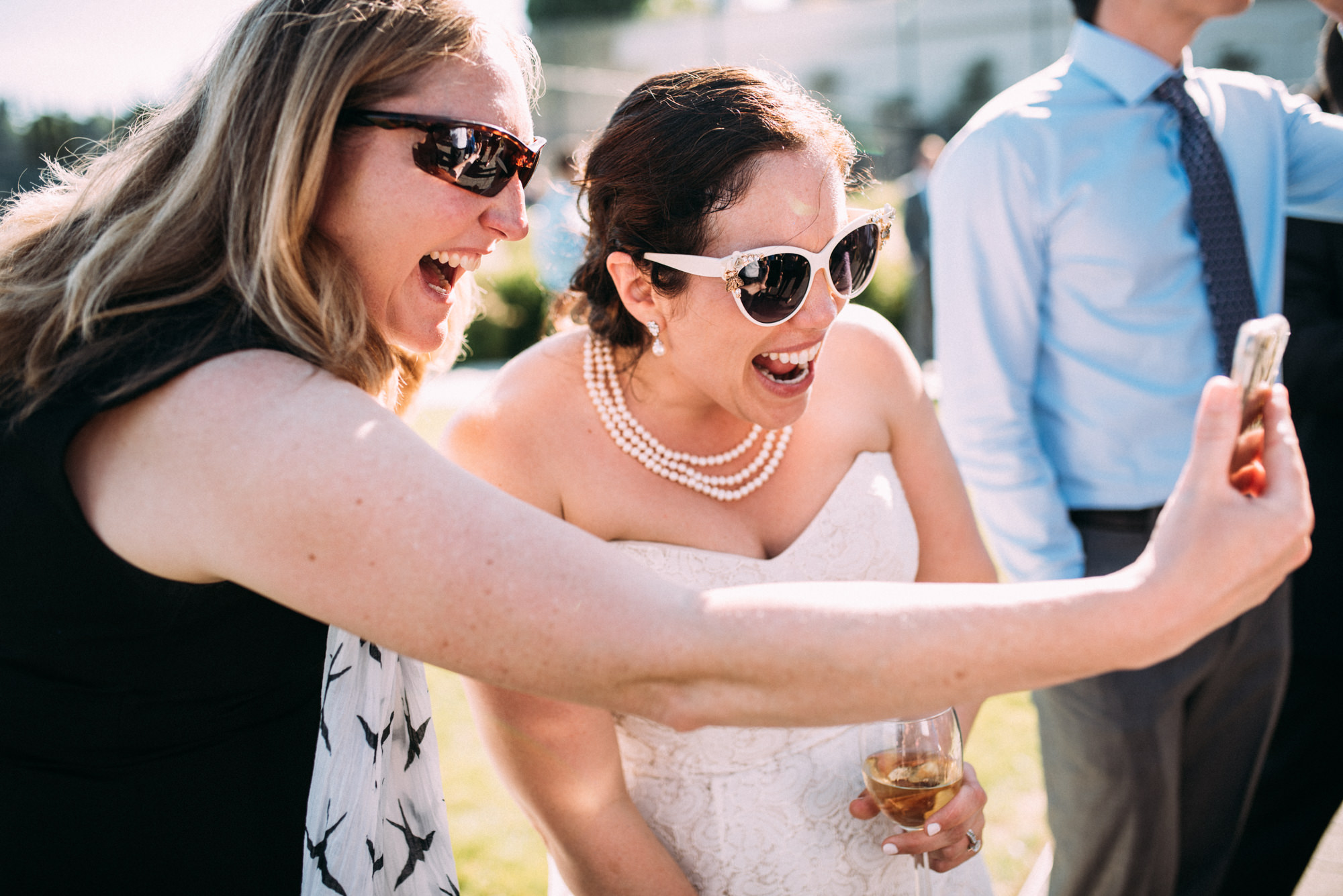 A guest facetimes with a friend and the bride at Joelle and Ryan's wedding cocktail reception at the Seattle Tennis Club. Summer 2016. Photo by Seattle Wedding Photographers Jennifer Tai Photo Artistry.