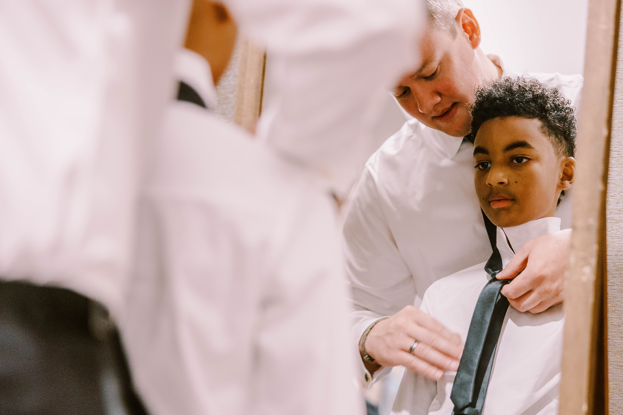 Groomsmen helps junior groomsmen tie his tie during getting ready