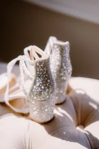 A pair of elegantly embellished bridal wedding shoes with glittering rhinestones and intricate beadwork, resting on a soft, creamy cushion under natural light.